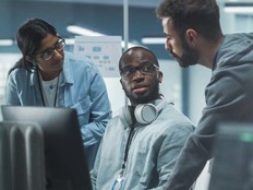 A group of professionals discuss something around some computers