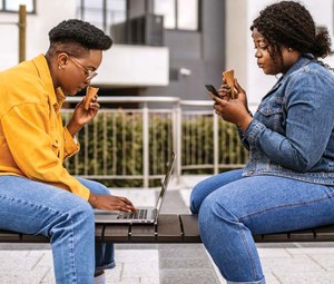 Two people sit on a bench while using their devices