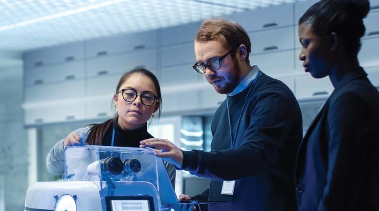 Three people inspect a robotics tool