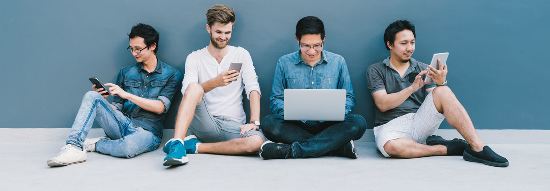four men using smartphone, laptop computer, digital tablet together with copy space on blue wall