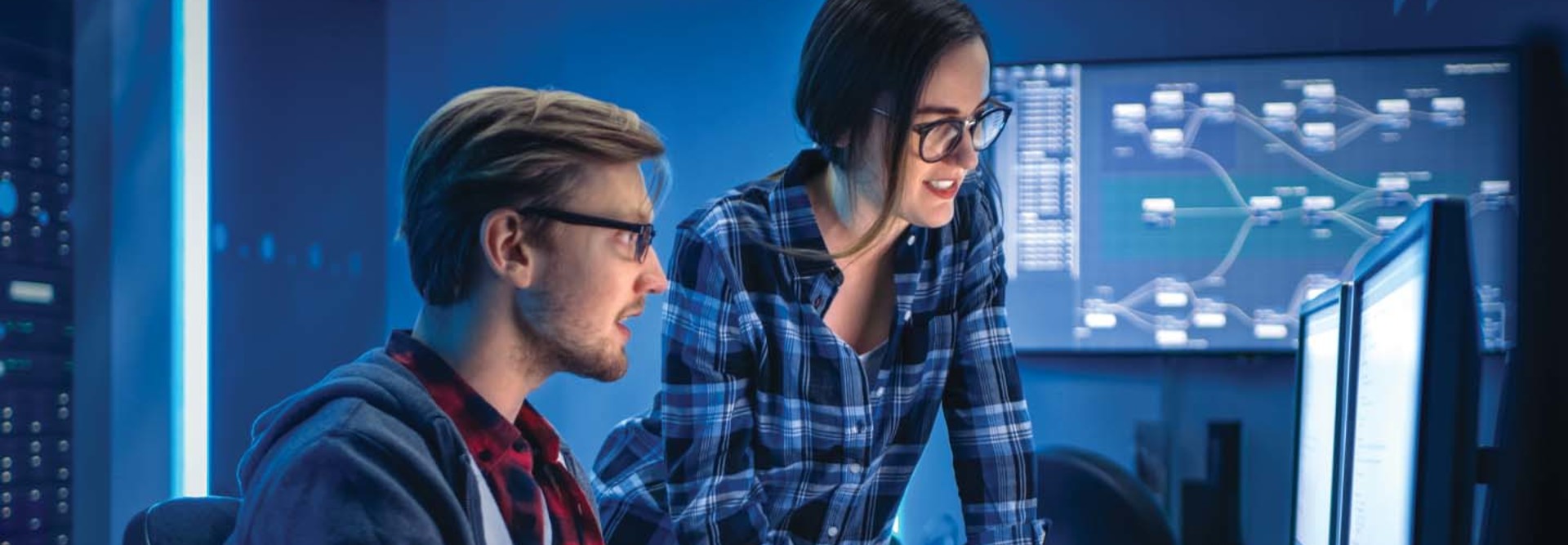 Two people look at a set of computer monitors
