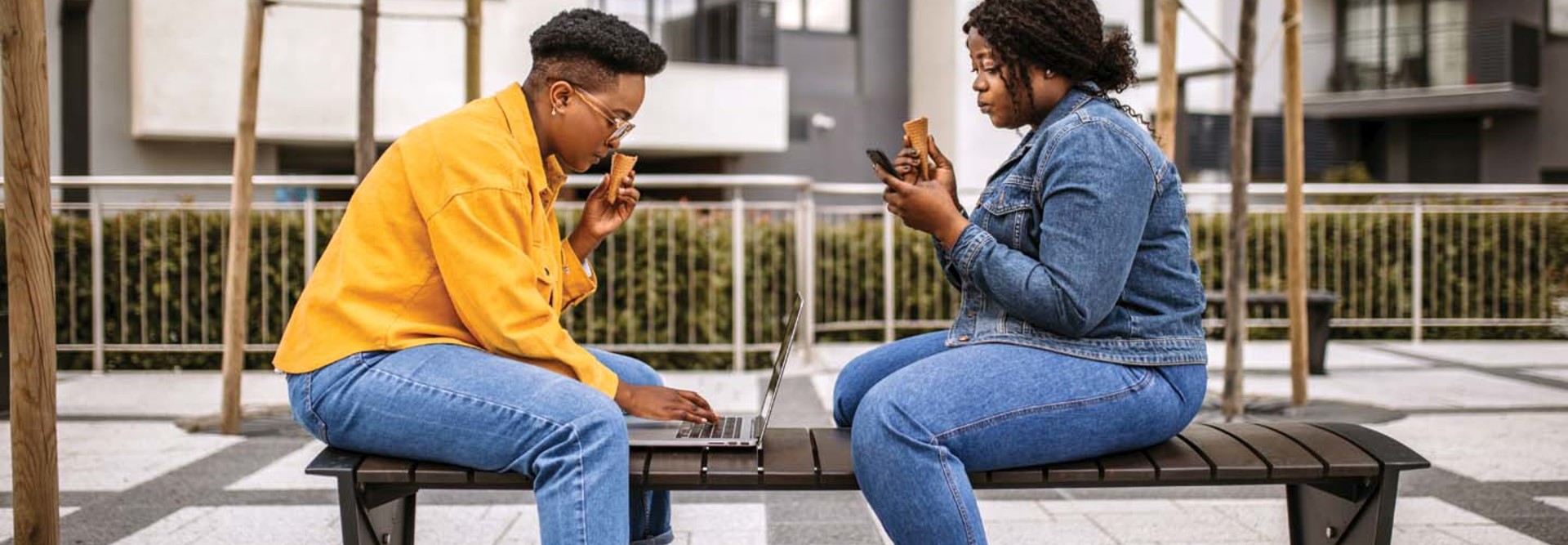 Two people sit on a bench while using their devices
