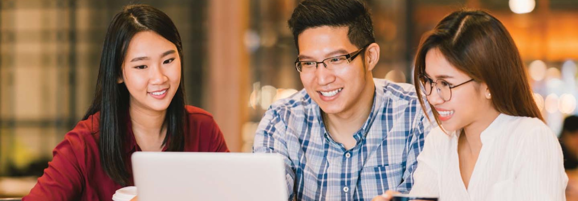 Three students look at a laptop