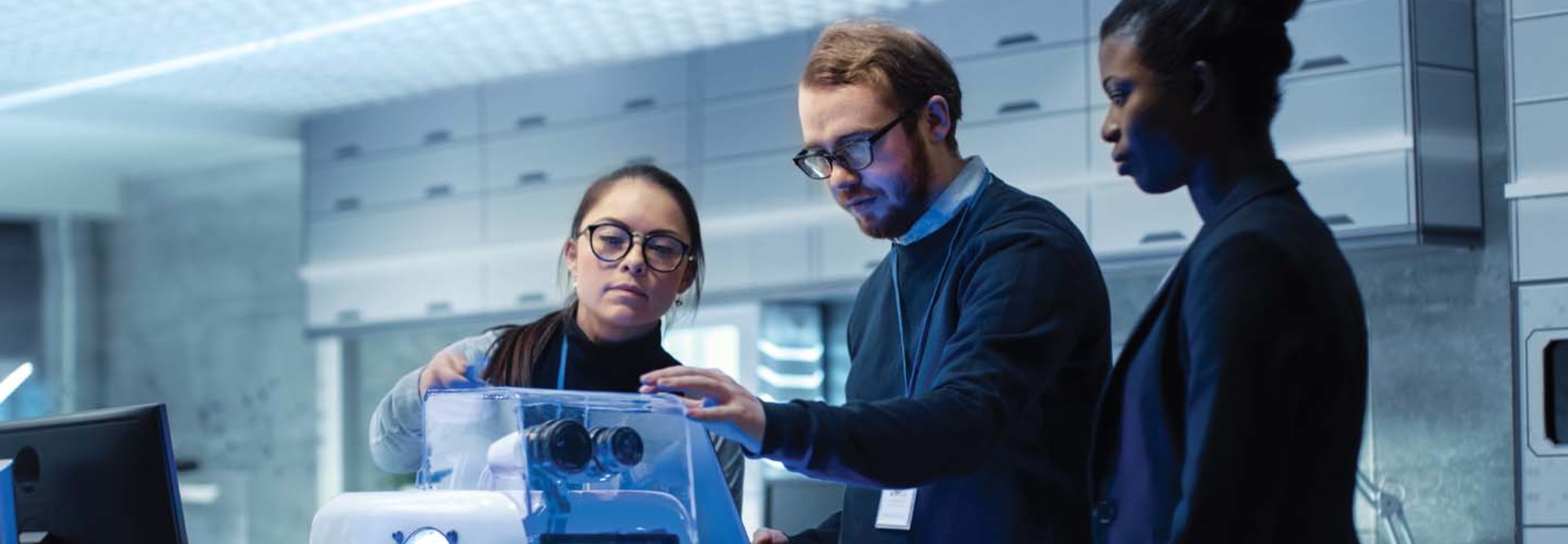 Three people inspect a robotics tool