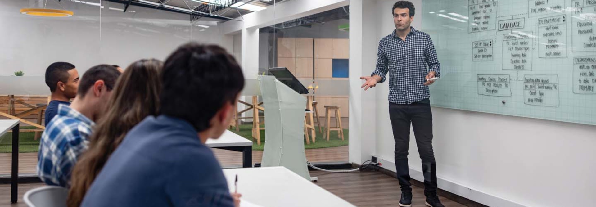 An instructor lectures from the front of a classroom
