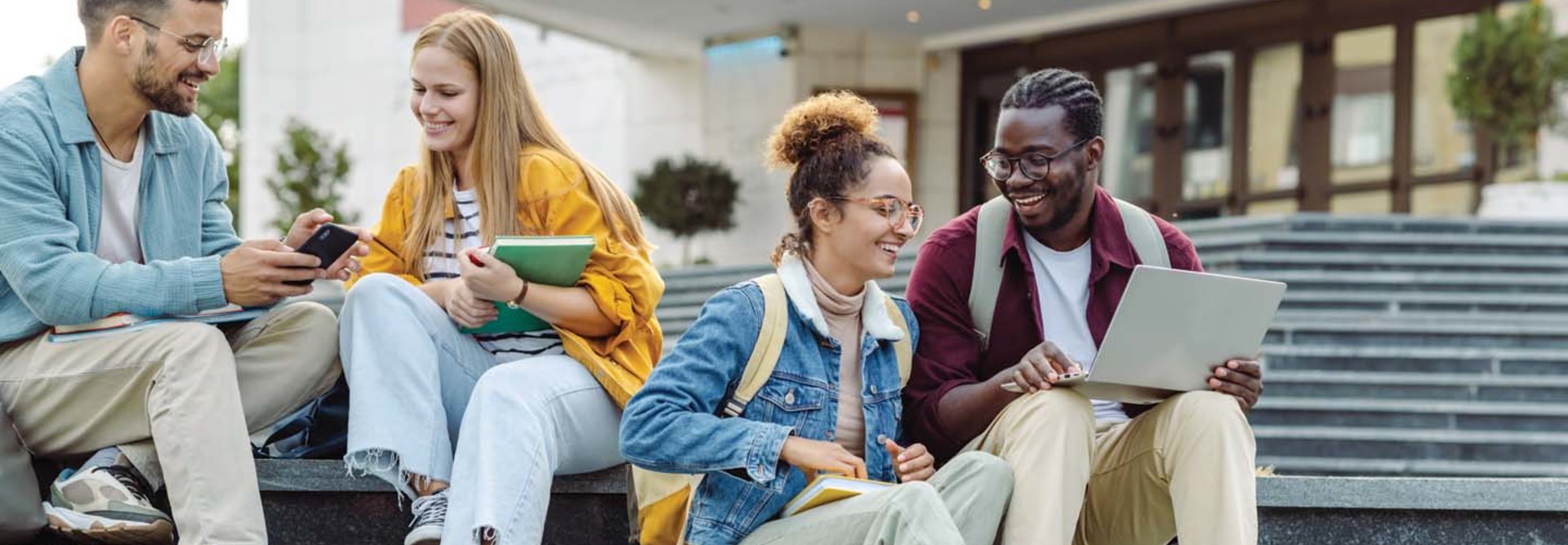 Students use their devices while sitting on the steps of a college building