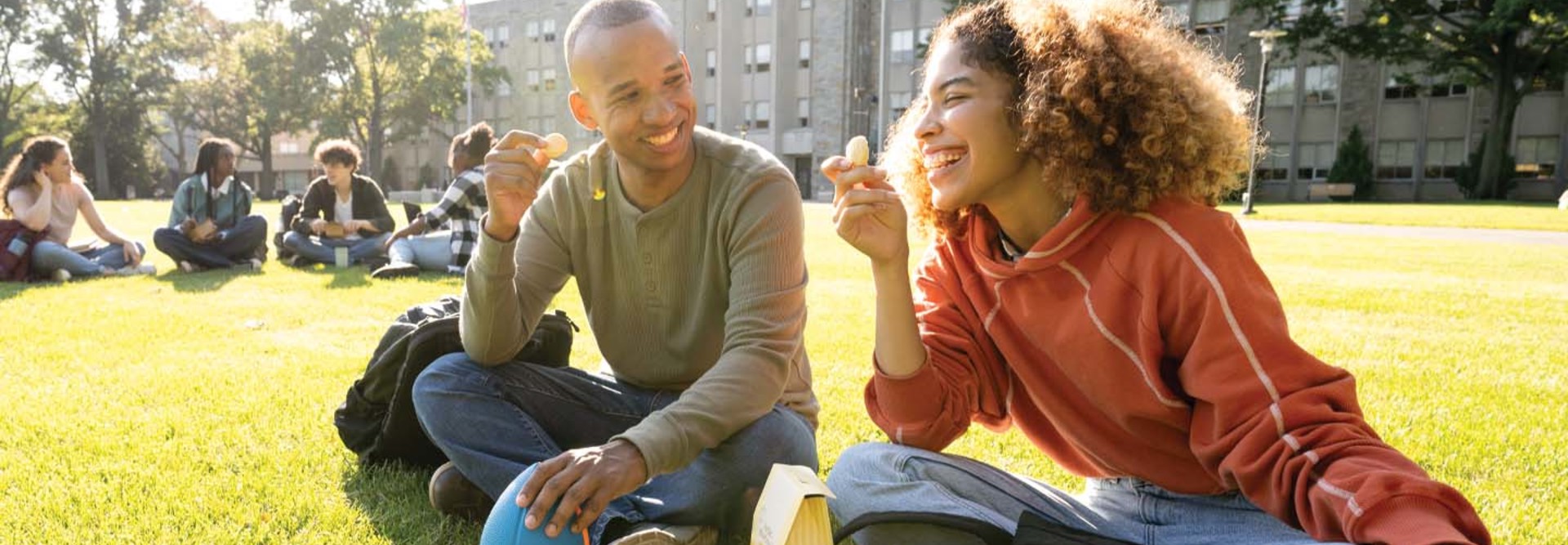 Two college students laugh while seated on a campus lawn