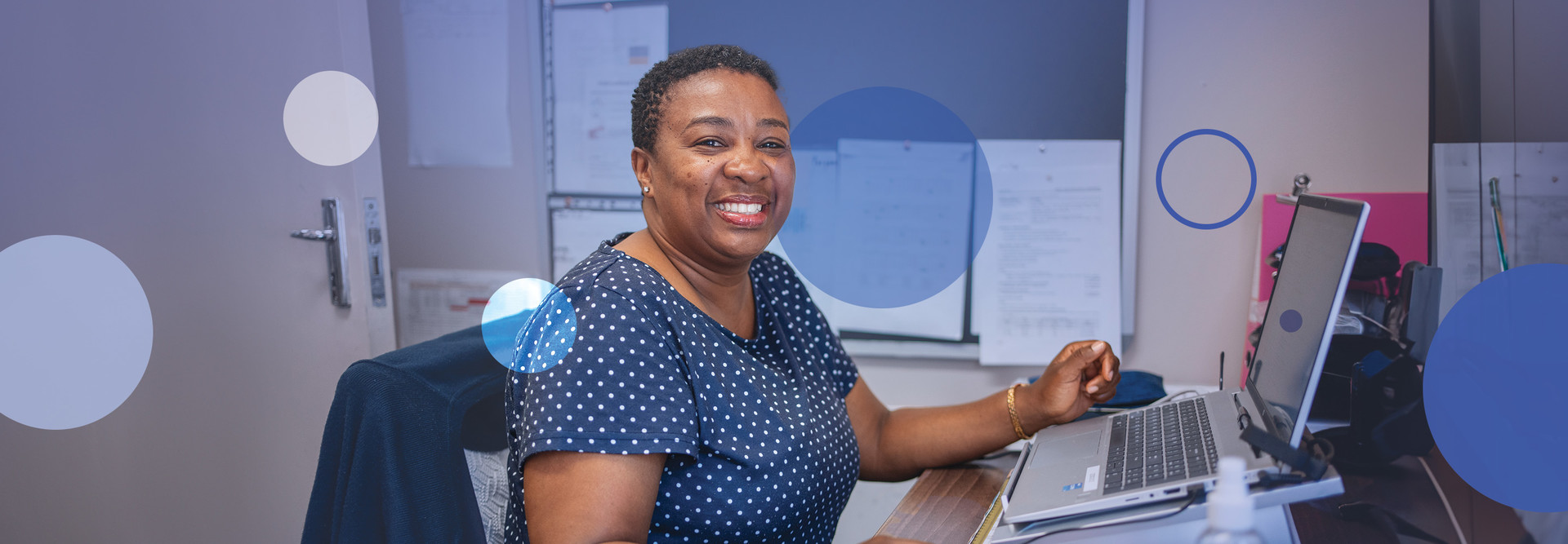 A woman smiles at the camera while working on her computer