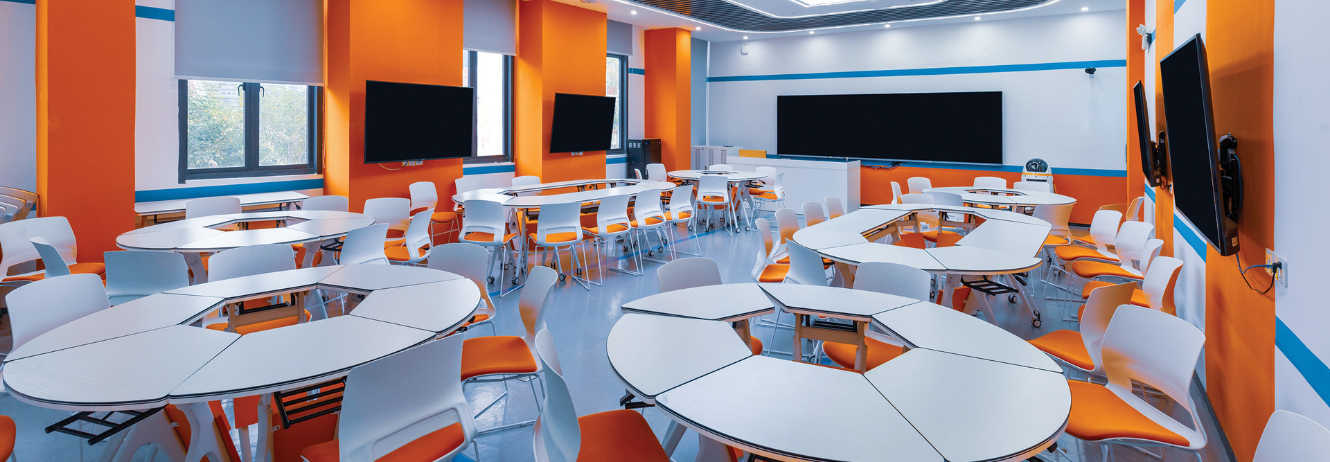 A modern college classroom with round tables and orange accent walls