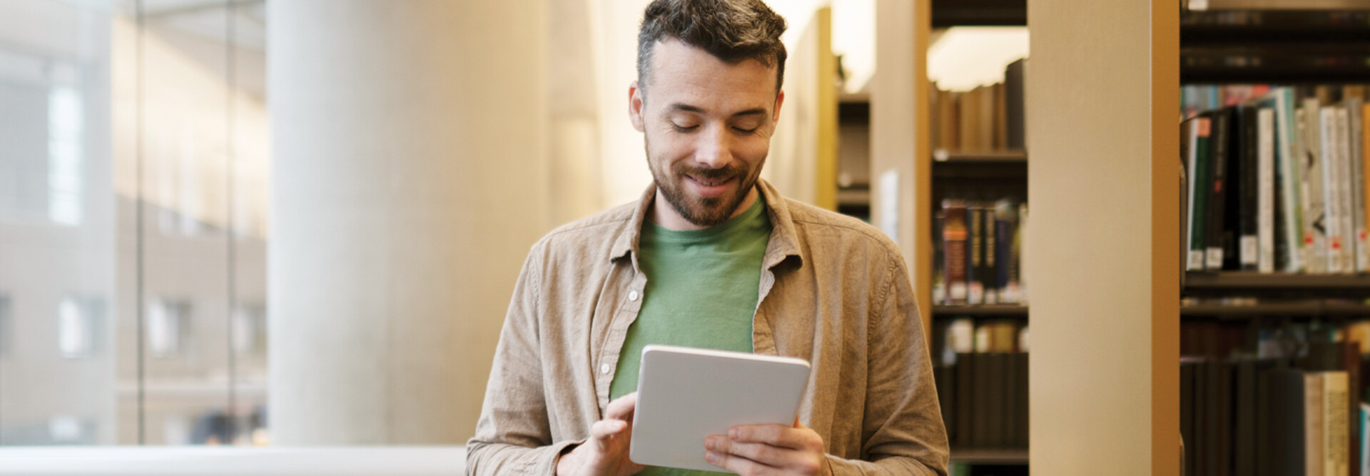A man looks at a tablet inside a library