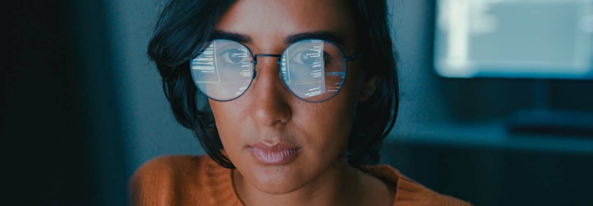 A woman's face with computer code reflected in her glasses
