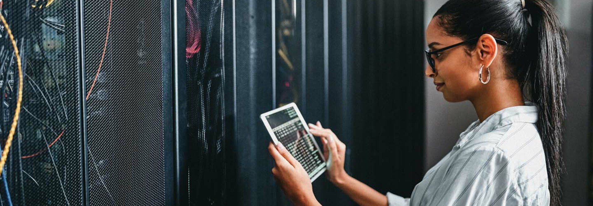 A woman holding a tablet inspects a cabinet of servers