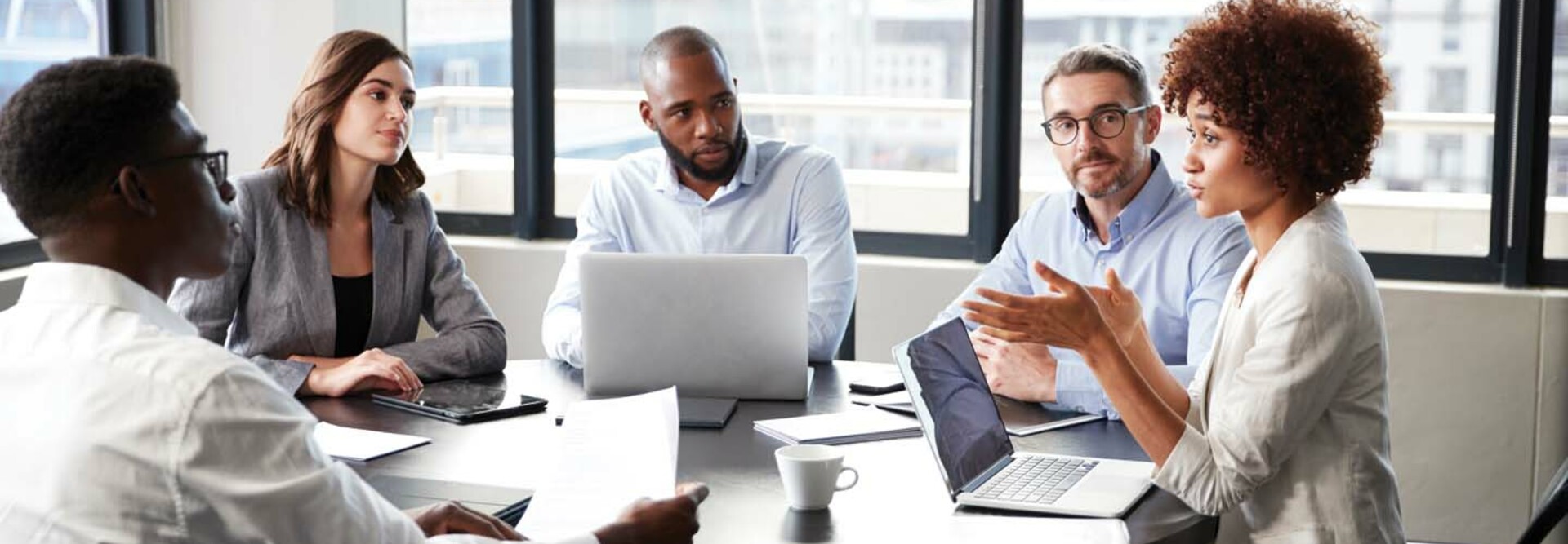 A group of people discuss something around a boardroom table