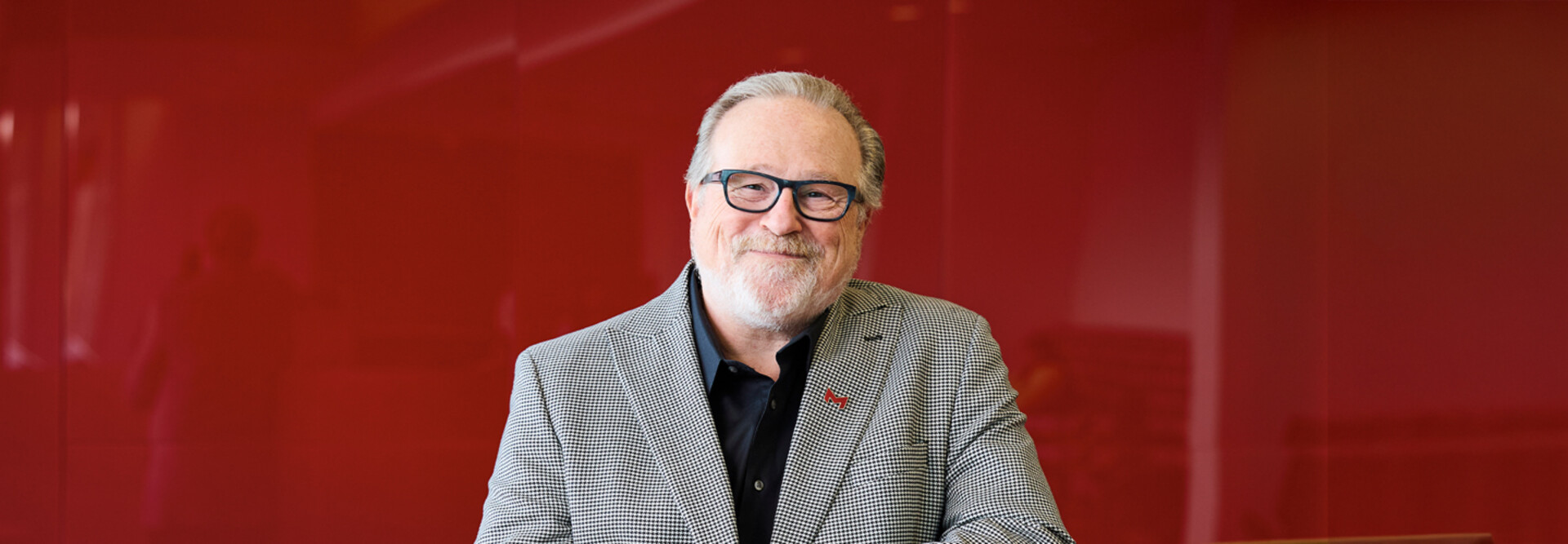 Maryville University President Mark Lombardi poses for a photo in front of a red background