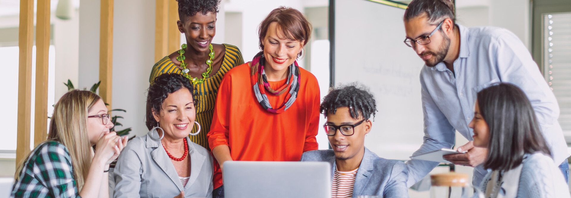 A group of smiling people gather around a laptop