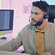 A man wearing a headset sits at a modern workstation with multiple monitors