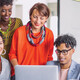 A group of smiling people gather around a laptop