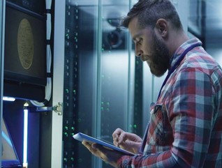 A man works on a tablet inside a large data center