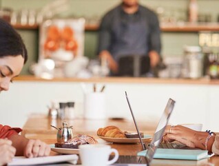 Two students work remotely in a coffee shop