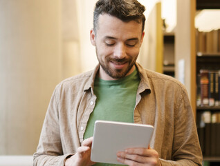 A man looks at a tablet inside a library