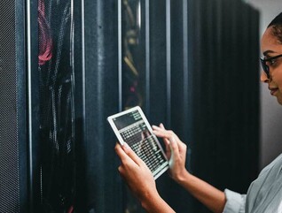 A woman holding a tablet inspects a cabinet of servers