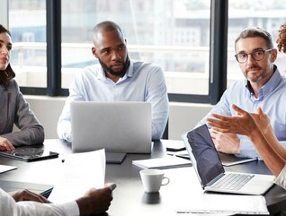 A group of people discuss something around a boardroom table