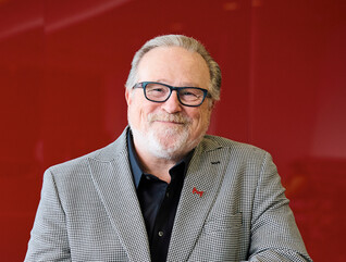 Maryville University President Mark Lombardi poses for a photo in front of a red background