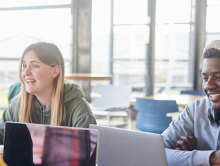 Diverse group of students smiling and studying at computers
