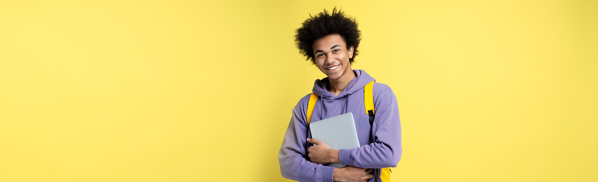 A man holding a laptop stands in front of a yellow background