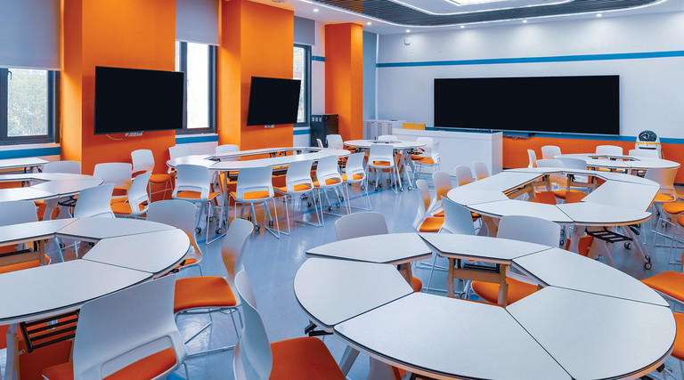 A modern college classroom with round tables and orange accent walls