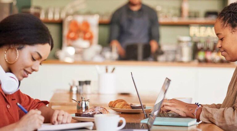Two students work remotely in a coffee shop