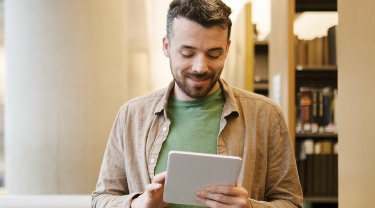 A man looks at a tablet inside a library