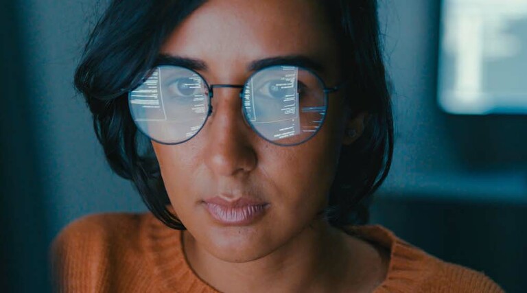 A woman's face with computer code reflected in her glasses