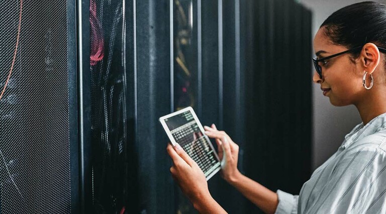 A woman holding a tablet inspects a cabinet of servers