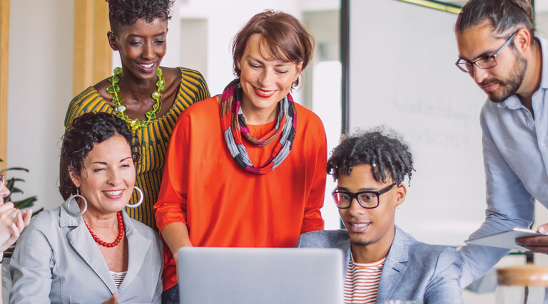 A group of smiling people gather around a laptop