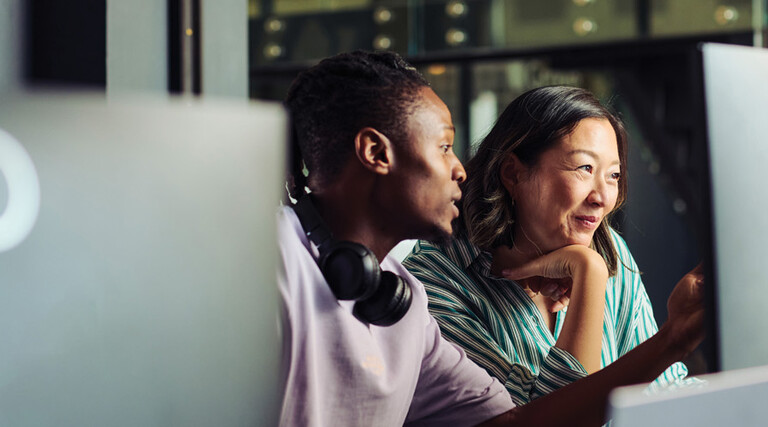 Two people work together at a desktop computer