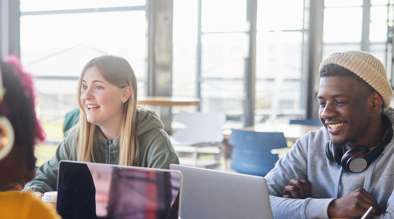 Diverse group of students smiling and studying at computers