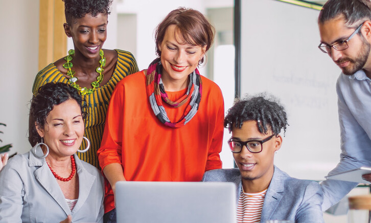 A group of smiling people gather around a laptop