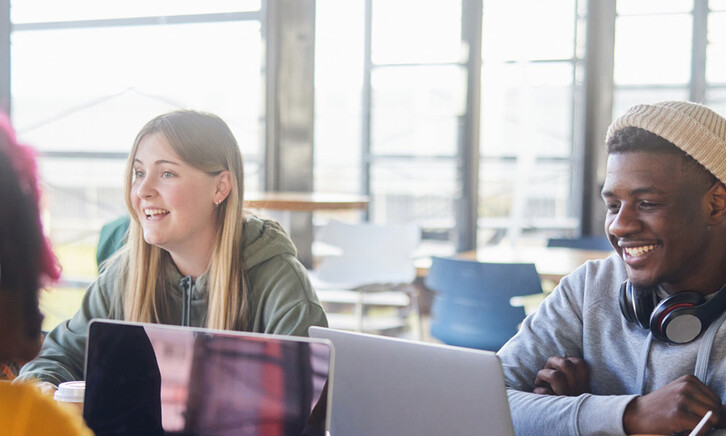 Diverse group of students smiling and studying at computers