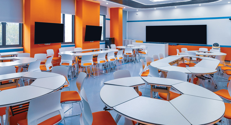 A modern college classroom with round tables and orange accent walls