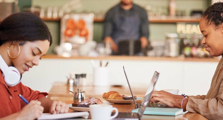 Two students work remotely in a coffee shop