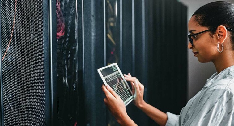A woman holding a tablet inspects a cabinet of servers
