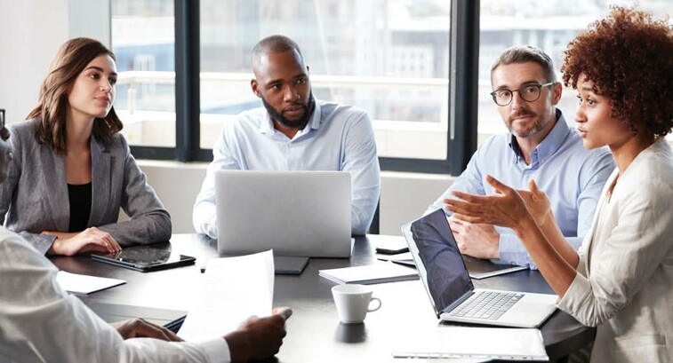 A group of people discuss something around a boardroom table