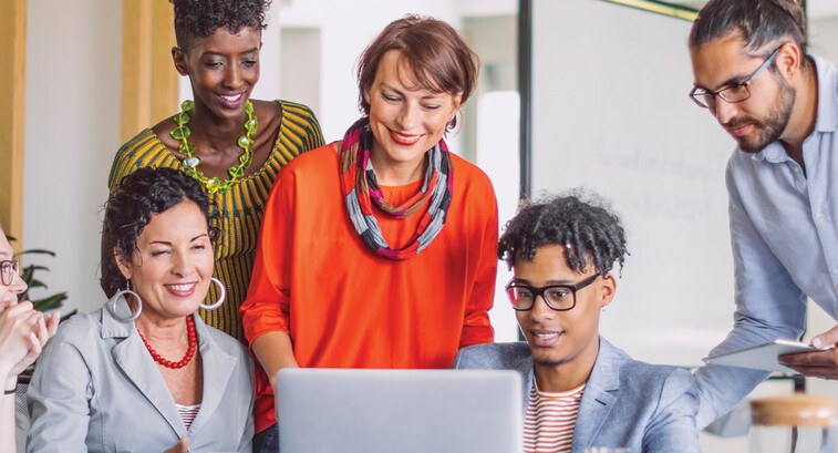 A group of smiling people gather around a laptop