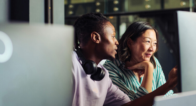 Two people work together at a desktop computer