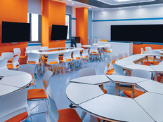 A modern college classroom with round tables and orange accent walls