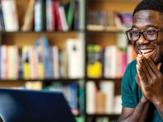 A young man reacts excitedly to a message on his laptop