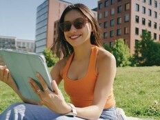A college student seated outdoors looks at a tablet