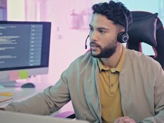 A man wearing a headset sits at a modern workstation with multiple monitors
