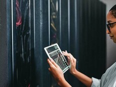 A woman holding a tablet inspects a cabinet of servers